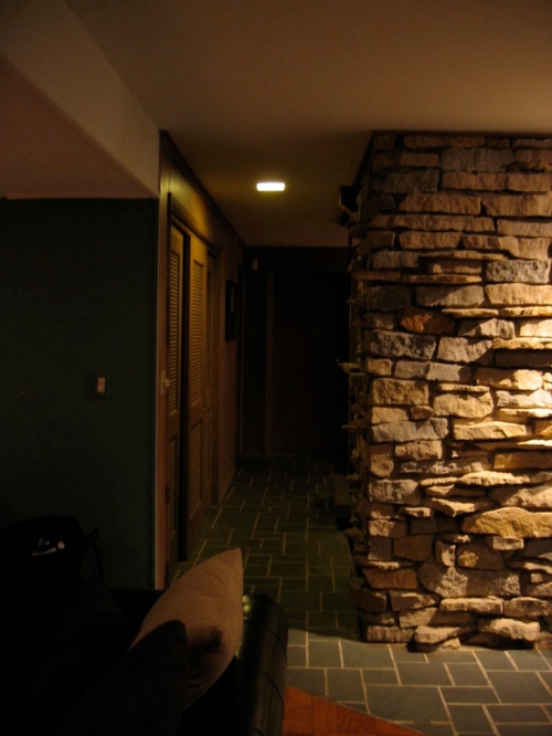 Living area downstairs at night; looking down hall toward foyer with bathroom and garage entry